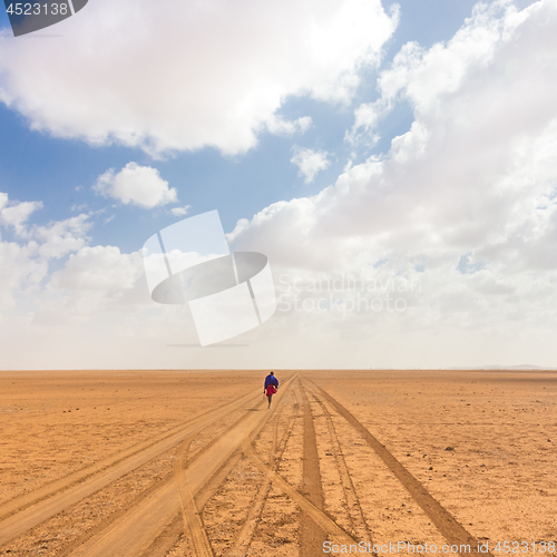 Image of Solitary masai worrior walking along salt lake desert road in Kenya, Amboseli Natural Park, Africa