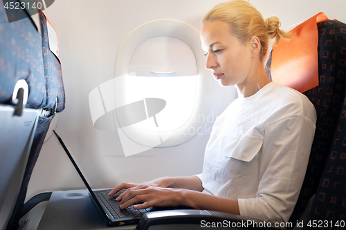 Image of Attractive caucasian female passenger working at modern laptop computer using wireless connection on board of commercial airplane flight