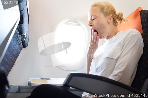 Image of Beautiful casual caucasian woman yawning on airplane flight while reading in flight magazine.