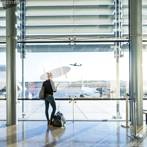 Image of Young woman waiting at airport, looking through the gate window.