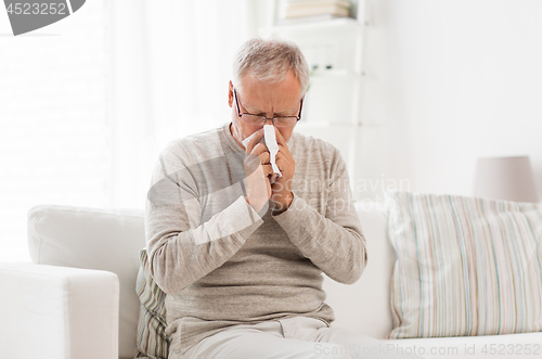 Image of sick senior man with paper wipe blowing his nose