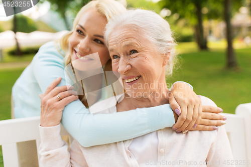 Image of daughter with senior mother hugging on park bench