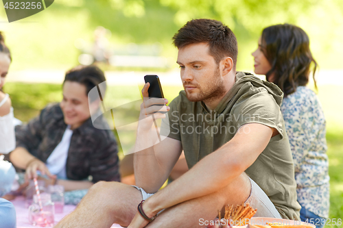 Image of man using smartphone at picnic with friends