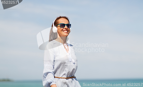Image of woman with headphones walking along summer beach