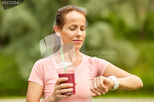 Image of woman with smoothie looking at smart watch in park