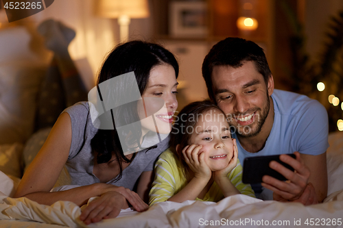 Image of happy family with smartphone in bed at night