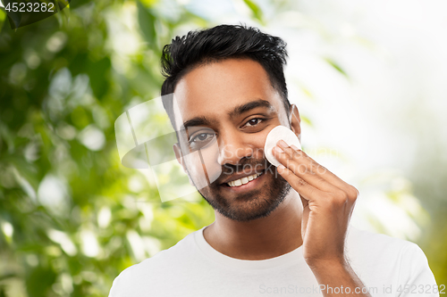 Image of smiling indian man cleaning face with cotton pad