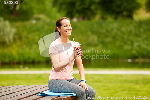 Image of woman drinking smoothie after exercising in park