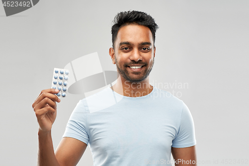 Image of smiling indian man with pills over grey background