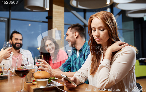 Image of bored woman messaging on smartphone at restaurant