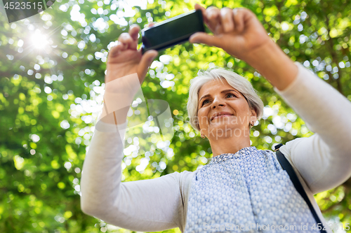 Image of senior woman photographing by cell at summer park