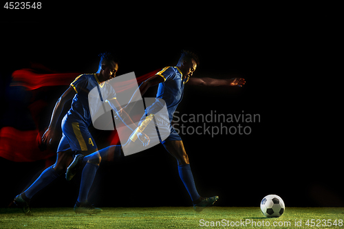 Image of Male soccer player kicking ball on dark background in mixed light