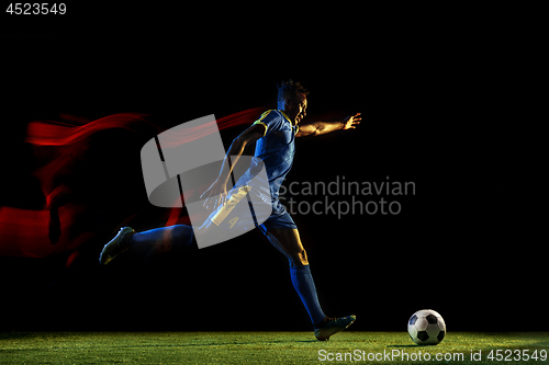 Image of Male soccer player kicking ball on dark background in mixed light