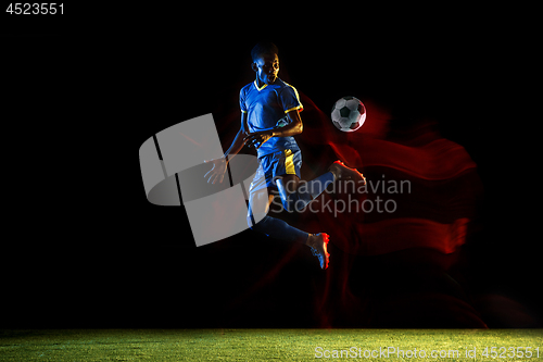 Image of Male soccer player kicking ball on dark background in mixed light