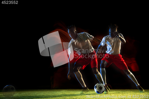 Image of Male soccer player kicking ball on dark background in mixed light