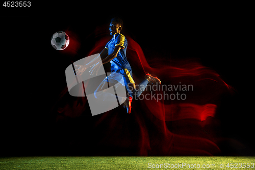 Image of Male soccer player kicking ball on dark background in mixed light