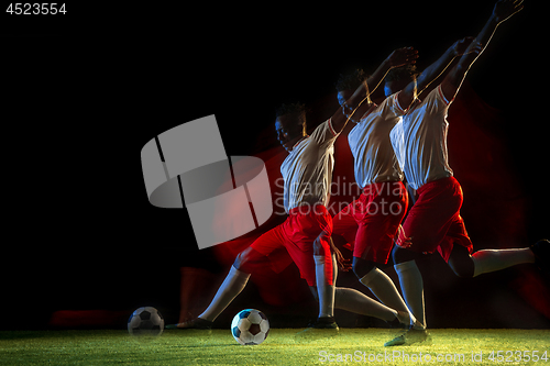 Image of Male soccer player kicking ball on dark background in mixed light