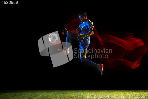 Image of Male soccer player kicking ball on dark background in mixed light