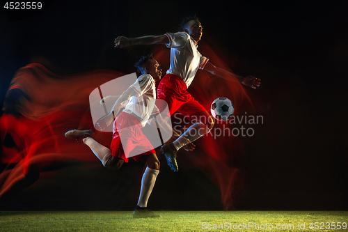 Image of Male soccer player kicking ball on dark background in mixed light