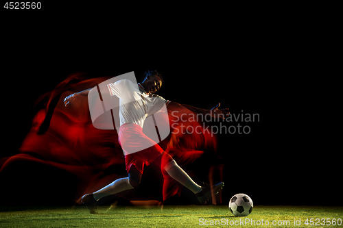 Image of Male soccer player kicking ball on dark background in mixed light