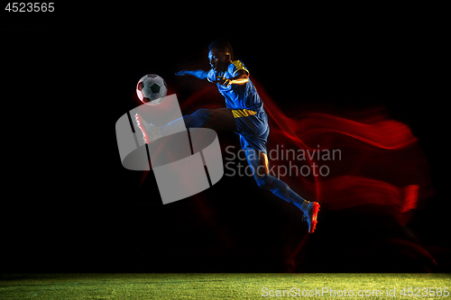 Image of Male soccer player kicking ball on dark background in mixed light