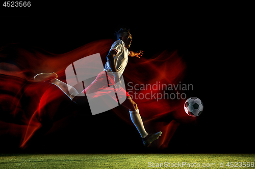 Image of Male soccer player kicking ball on dark background in mixed light