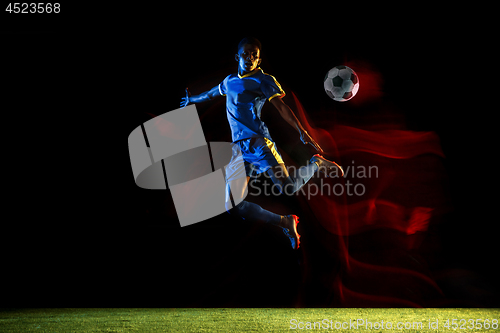 Image of Male soccer player kicking ball on dark background in mixed light