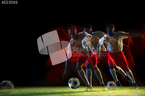 Image of Male soccer player kicking ball on dark background in mixed light