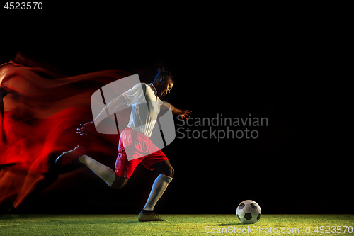 Image of Male soccer player kicking ball on dark background in mixed light