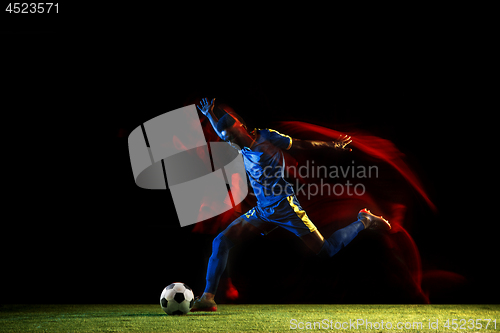 Image of Male soccer player kicking ball on dark background in mixed light