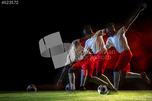 Image of Male soccer player kicking ball on dark background in mixed light