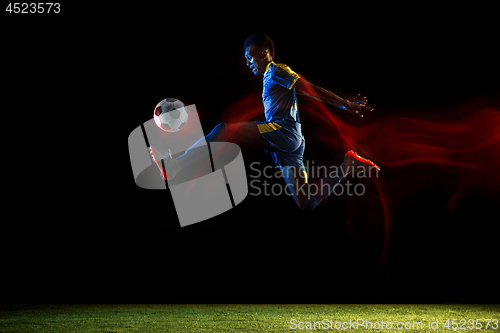 Image of Male soccer player kicking ball on dark background in mixed light