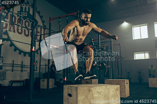 Image of Man jumping during exercises in the fitness gym. CrossFit.