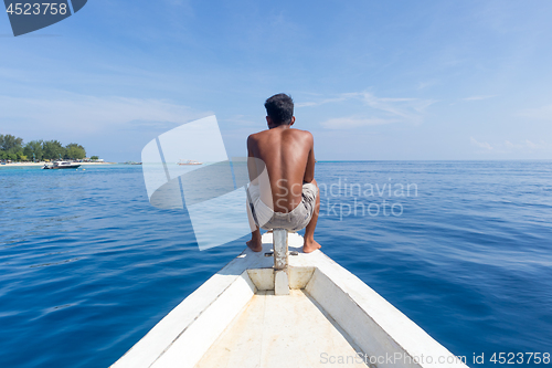 Image of Local Sporty Guy Sitting Topless at the Bow of Traditional White Wooden Sail Boat, Looking At Beautiful Blue Sea of Gili Islands near Bali, Indonesia