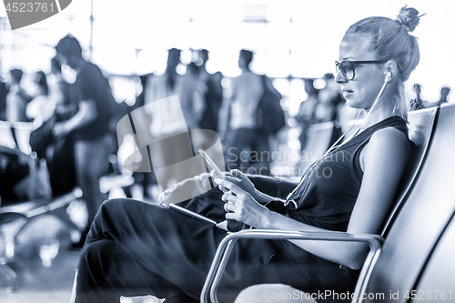 Image of Female traveler using her cell phone while waiting to board a plane at departure gates at asian airport terminal. Blue toned black and white photo.