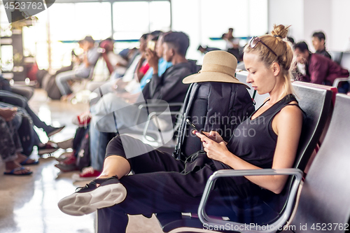 Image of Female traveler talking on cell phone while waiting to board a plane at departure gates at asian airport terminal.