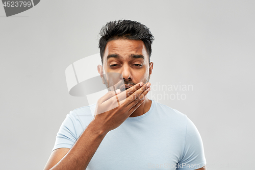 Image of tired indian man yawning over grey background