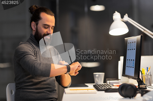 Image of man with smartwatch and computer at night office