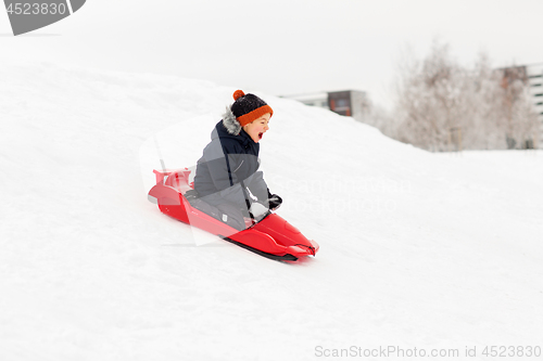 Image of happy boy sliding on sled down snow hill in winter