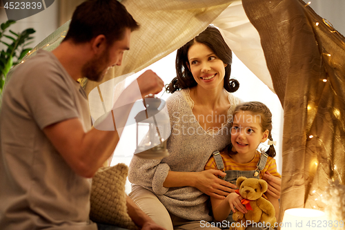 Image of happy family playing in kids tent at night at home