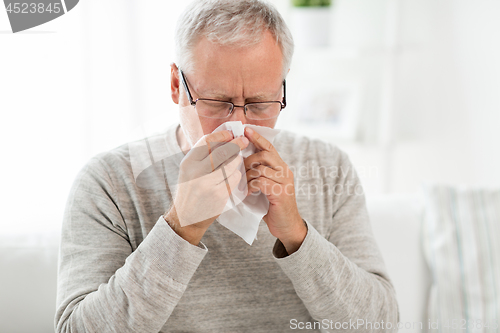 Image of sick senior man with paper wipe blowing his nose