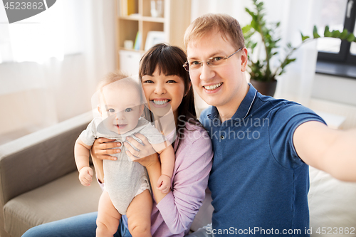 Image of mixed race family with baby taking selfie at home