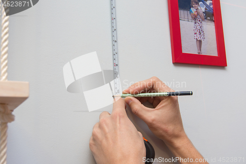 Image of Hands mark out on the wall the arrangement of frames with photos