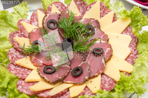 Image of Sliced on a plate of sausage and cheese, decorated with greens and olives