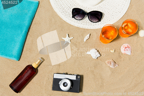 Image of drinks, hat, camera and sunglasses on beach sand