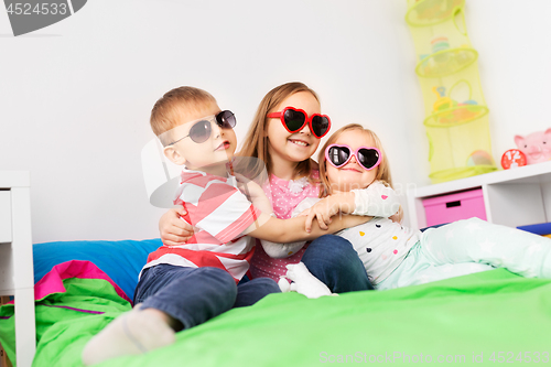 Image of happy little kids in sunglasses hugging at home