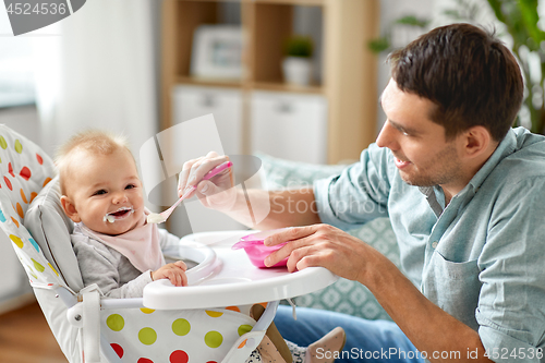 Image of father feeding happy baby in highchair at home