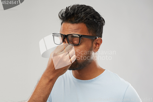 Image of tired indian man in glasses rubbing nose bridge