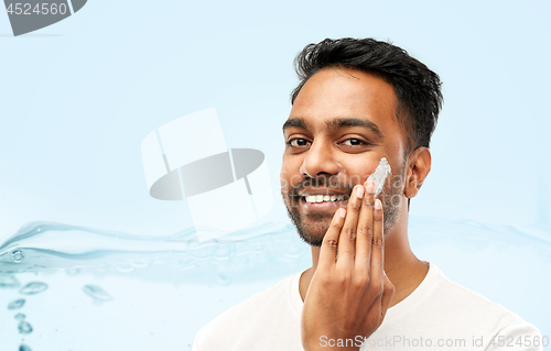 Image of happy indian man applying cream to face