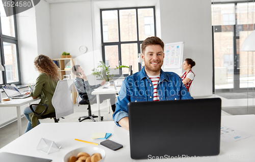 Image of smiling creative man with laptop working at office